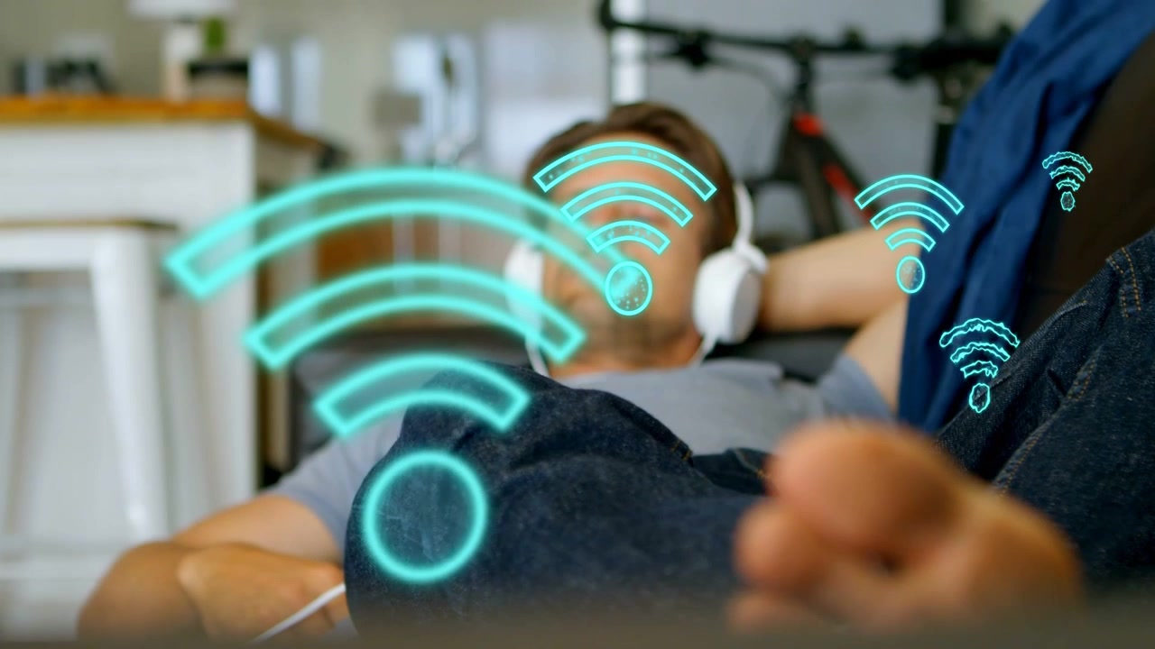 Uomo sdraiato con le cuffie in riproduzione, il piede in primo piano mostra icone WiFi crescenti a suggerire la connessione