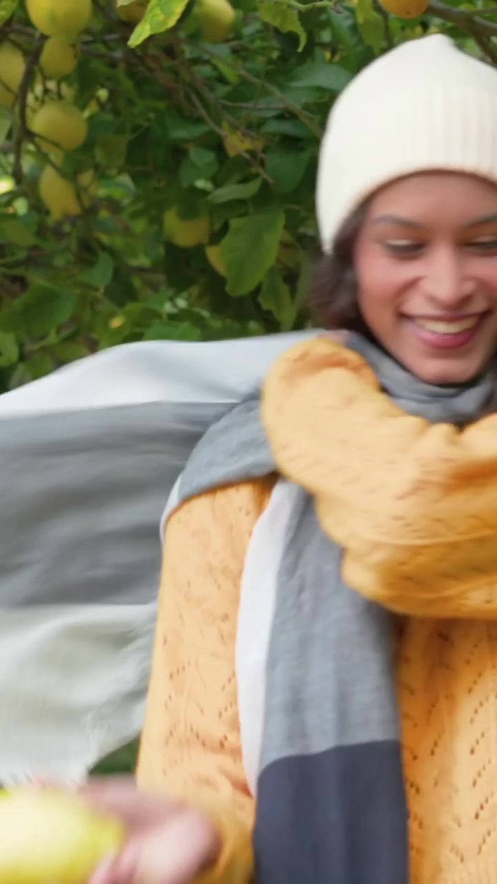 Video verticale: Uomo appoggiato che spinge leggermente una donna in maglia gialla che sistema la sciarpa vicino a un albero in giardino, spazio per il testo.