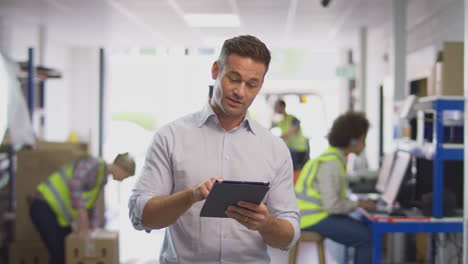 gerente masculino en un almacén de distribución de logística ocupado usando una tableta digital