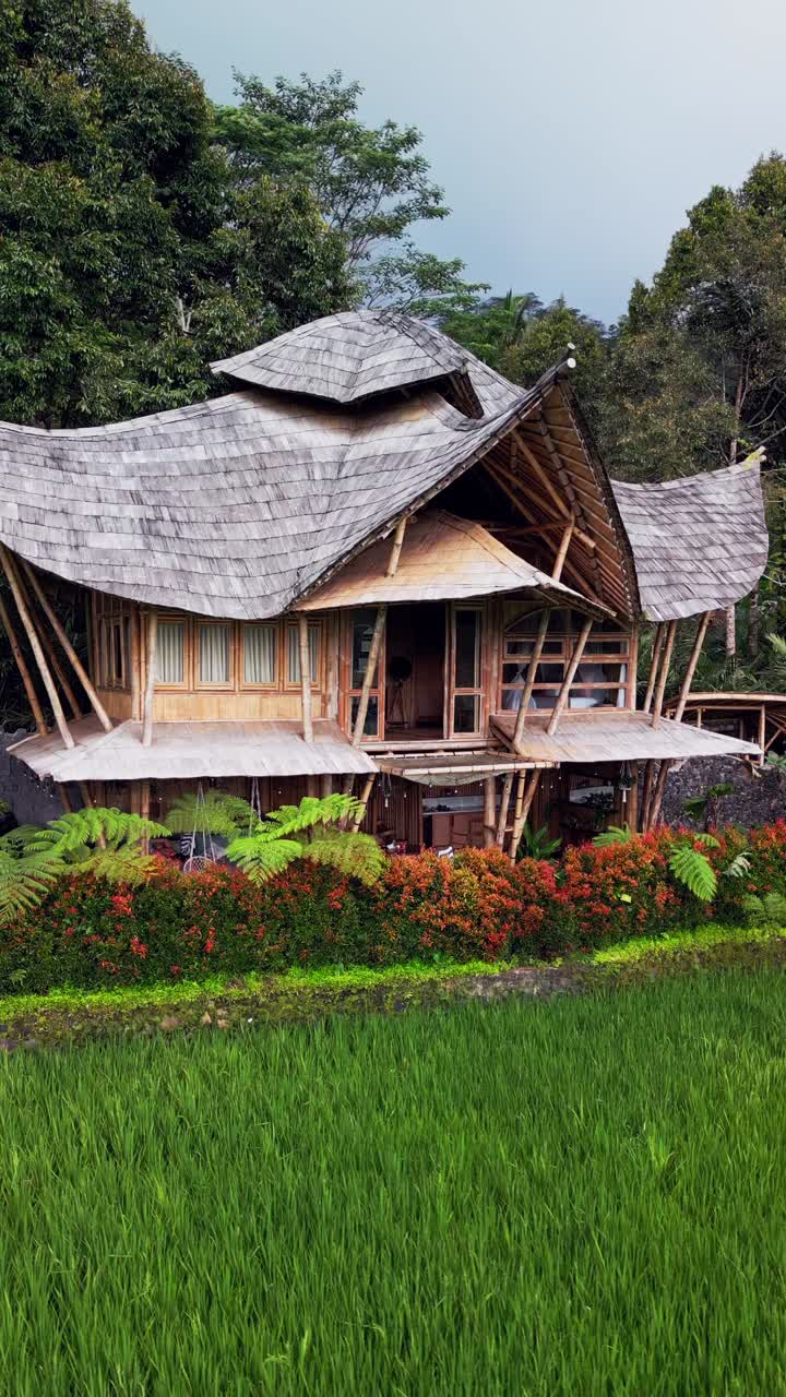 Vertical drone footage of a bamboo house in Sidemen Bali surrounded by rice paddies and tropical forest, showcasing Balinese craftsmanship, peaceful scenery, and sustainable island living design