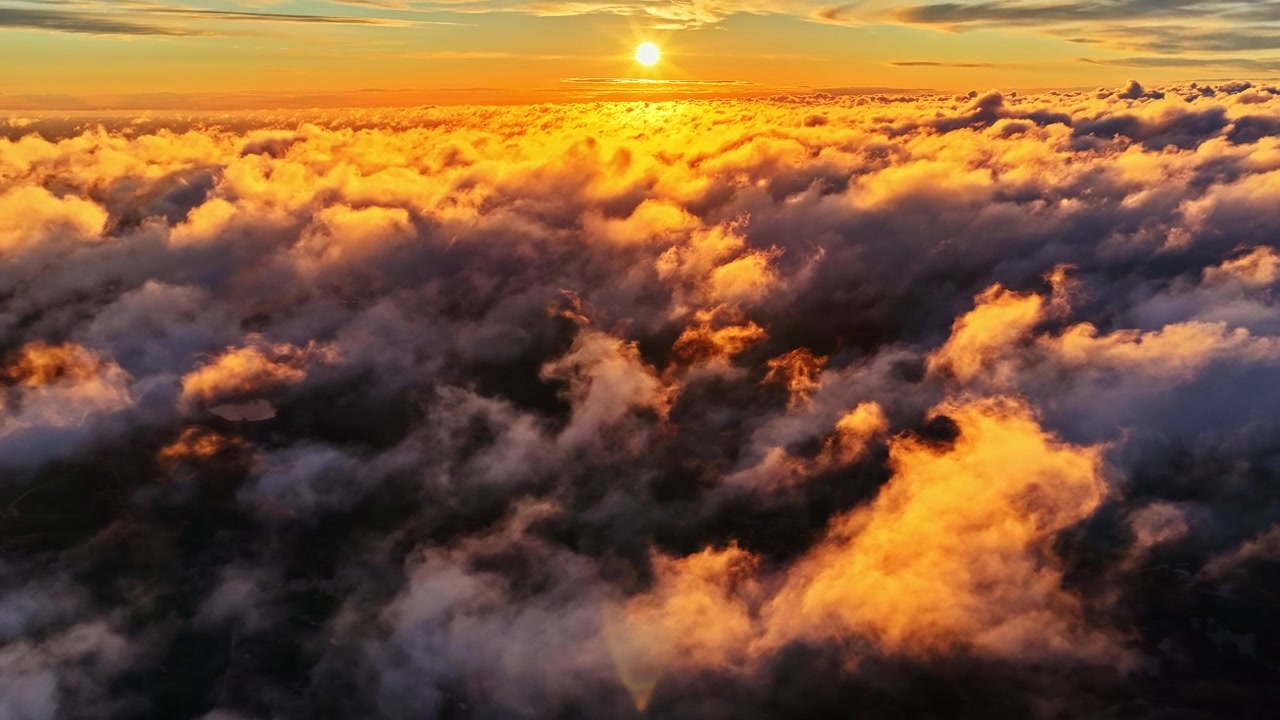 Breathtaking high-angle shot looking out over a thick sea of clouds during a dramatic sunset. Features blazing bands of orange, yellow, and red light painted across an expansive sky horizon.