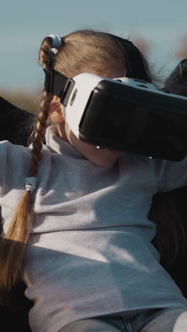 niña pequeña en auriculares vr gira las manos controlando los movimientos del personaje del juego. niño preescolar se divierte sentado en silla de ruedas en primer plano de fondo borroso