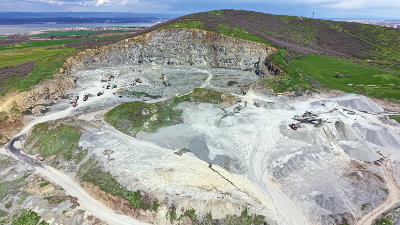 Granite quarry sits on a hillside with heavy machinery working during the day under a clear sky