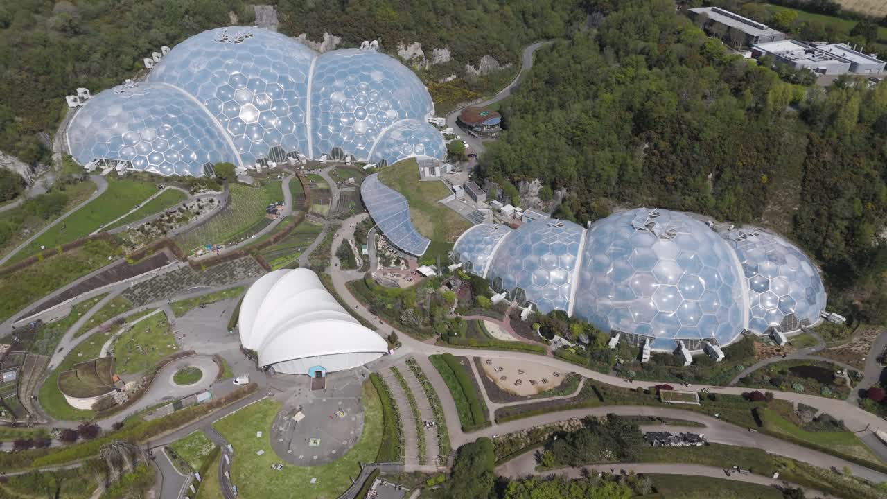 High-altitude view of Eden Project geodesic domes gleaming amid concentric botanical zones and wooded quarry slopes, emphasising innovative biomes and environmental stewardship