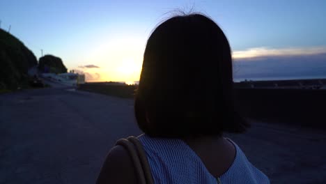 camera following back of short haired female walking at dusk with sunset light behind her slow motion