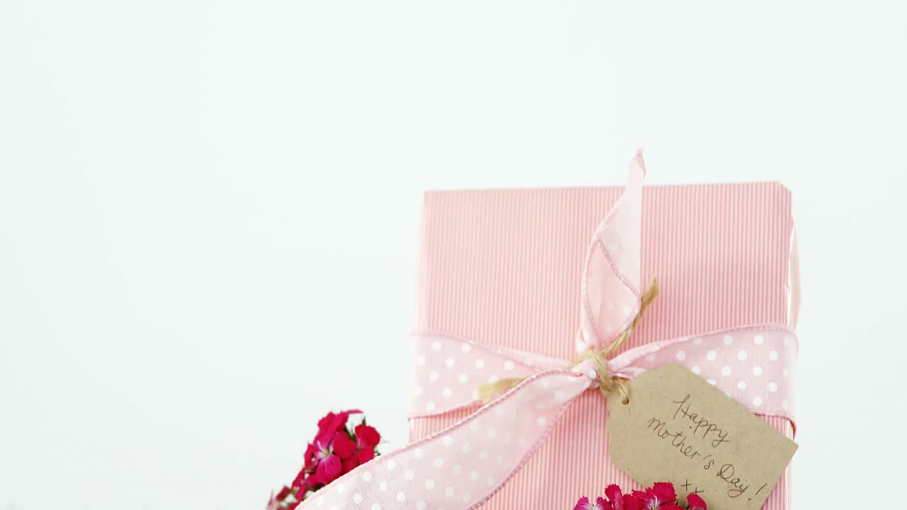 Scatola regalo con etichetta 'Buona Festa della Mamma' e fiori sull'erba