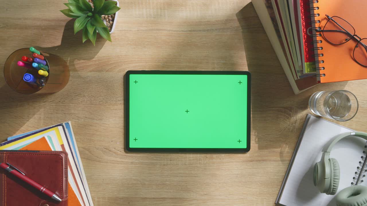 vista de arriba hacia abajo de una computadora portátil con pantalla verde simulada pantalla chromakey en un escritorio de oficina de madera al lado de la libreta con bolígrafos, gafas y un vaso de agua.