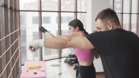 young athletic woman in a fistical gloves is training boxing in a fitness room with her male couch