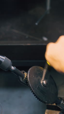 cu: experienced goldsmith turns handle of coiling tool with shiny metal wire at workplace in craft workshop close view