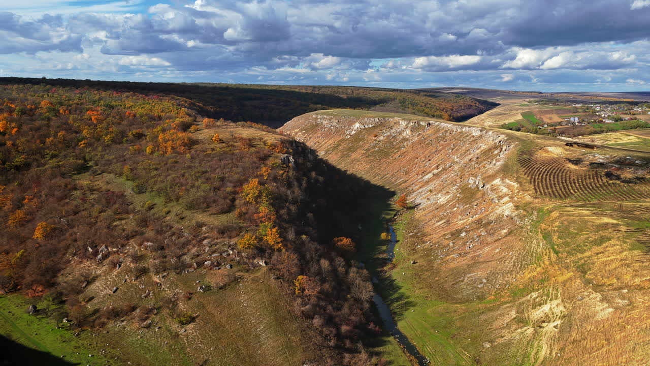 Aerial drone view of Moldova's hilly canyon landscape, with patches of autumn trees and winding trails