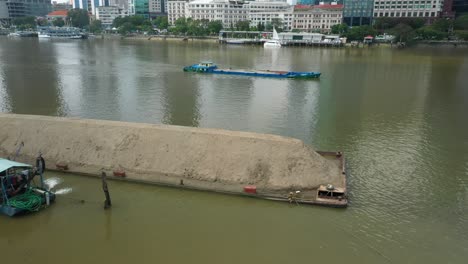 Toma-Aérea-Del-Paseo-Marítimo-De-La-Ciudad-De-Ho-Chi-Minh-Con-Remolcadores,-Barcazas-Y-Otros-Barcos-Que-Trabajan-En-El-Río-Saigón