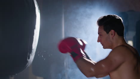 boxeador masculino fuerte golpeando la bolsa de boxeo mientras hace ejercicio