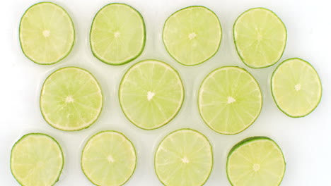 on a white background sliced pieces of lime are sprinkled with water. juicy fresh lime in slow motion. lots of lime slices.