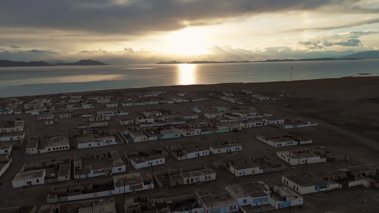 Aerial view of Karakul Lake in Tajikistan at sunset, showing the remote village on the shore and the Pamir Mountains in the background, one of Central Asia’s highest plateaus