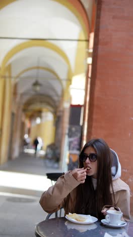 woman eating pastry and drinking coffee in an outdoor cafe