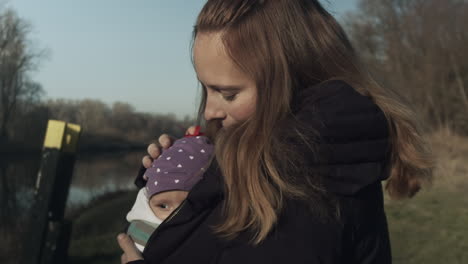 Mother-cradles-baby-wrapped-warmly-on-chest-outdoors,-slow-mo