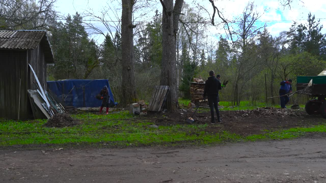 Fast-motion footage of people raking leaves and loading them onto a tractor during spring day at a Hageri countryside homestead, Estonia. Timelapse captures seasonal farm work and rural life teamwork