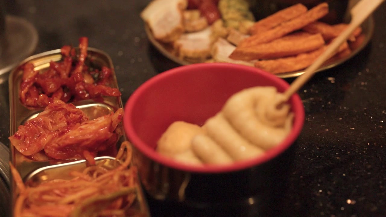 Primo piano di zuppa coreana di kimchi, pancetta di maiale e snack tempura su un tavolo scuro.