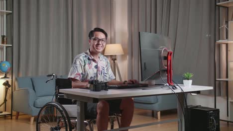 hombre asiático sonriente en silla de ruedas trabajando en casa