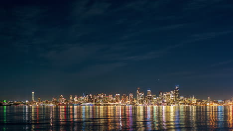 timelapse of seattle's illuminated skyline at night, with the iconic space needle and skyscrapers reflecting on the calm waters of elliott bay.