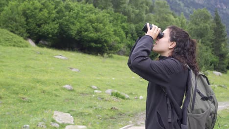 Adventurous-girl-looking-through-the-binoculars-in-search-of-birds-in-a-natural-mountain-environment