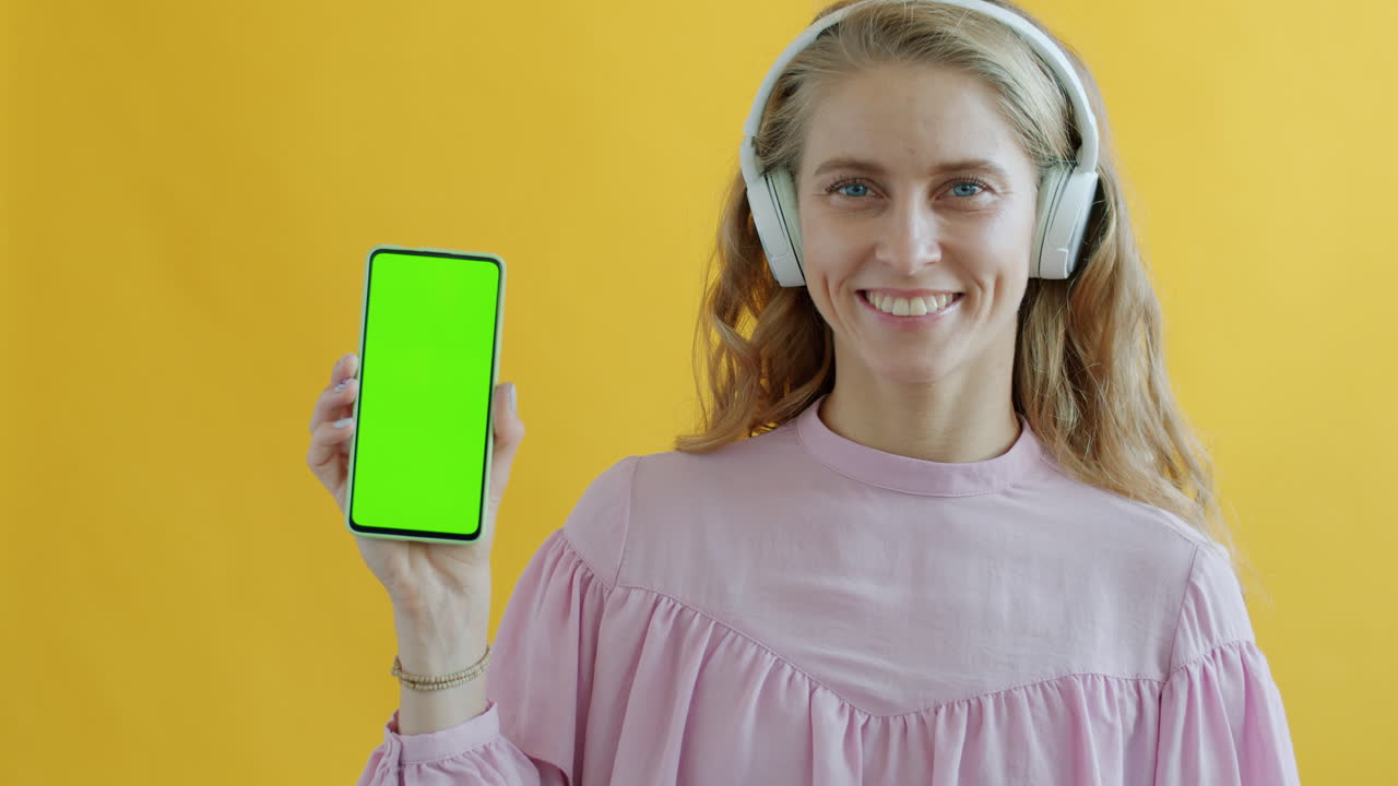 Woman with headphones holding a phone with green screen
