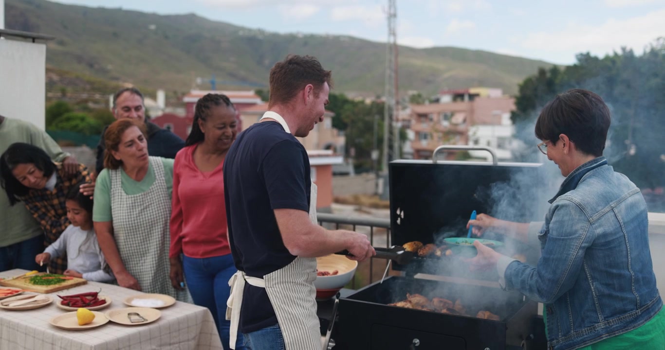 Amici e famiglia felici di diverse etnie che grigliano su una terrazza sul tetto