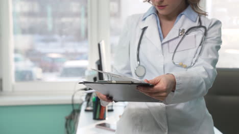 Concentrated-Female-Doctor-Checking-Medical-Report-In-Her-Consulting-Room