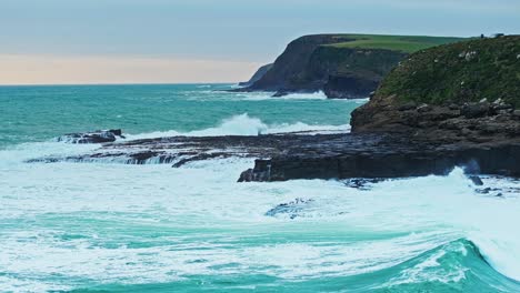 waves crash and build powerful sprays along rocky shoreline under overcast sky