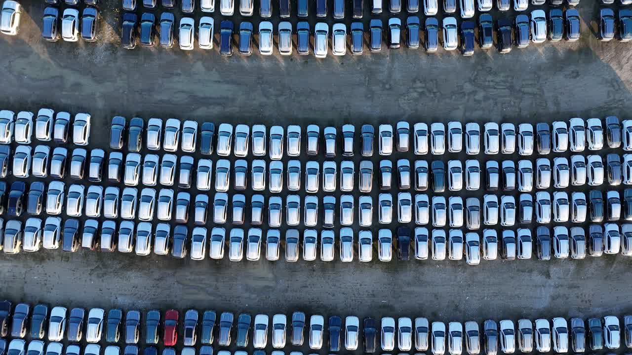 Aerial view of automotive logistics depot with rows of imported cars awaiting distribution, import staging areas near ports or terminals, Vehicles likely awaiting inspection, paperwork, transport