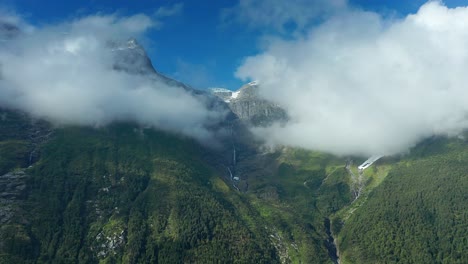 pan motion flight revealing the thick clouds covered mountain tops and waterfalls rush down the forest-covered slope