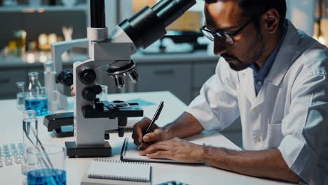 scientist working in a laboratory with a microscope and taking notes