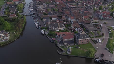 Wide-view-of-Woudsend-Friesland-village-with-sail-boat-cruising-during-sunset,-aerial