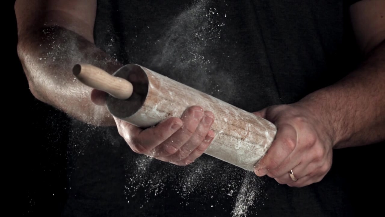 Handen kloppen bloem af van een houten deegroller in slow motion