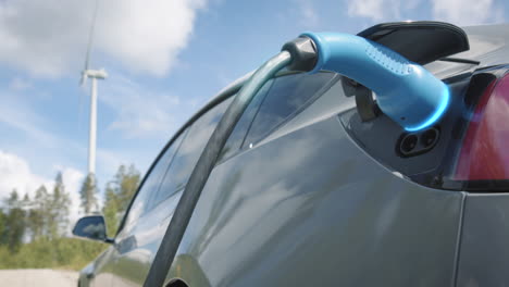 zoom in, graphics enhanced - a generic electric car charges in front of a wind turbine