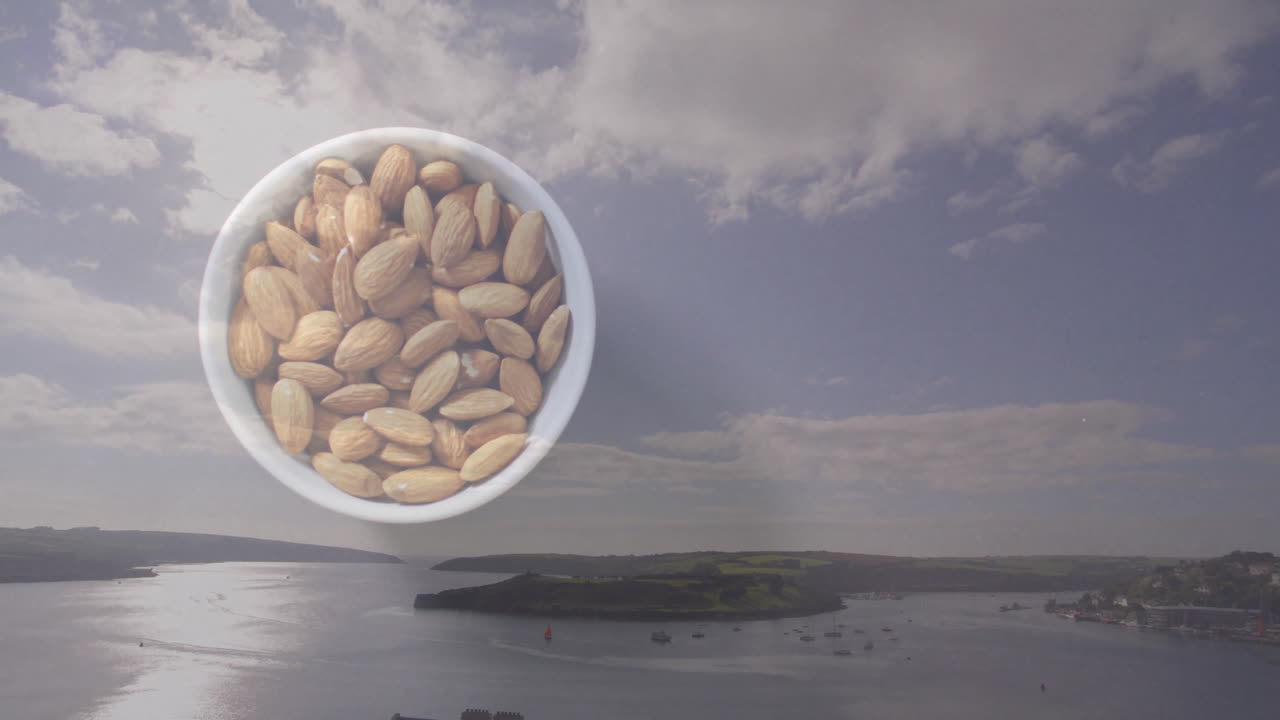 Almonds in bowl with animation of serene coastal landscape and cloudy sky
