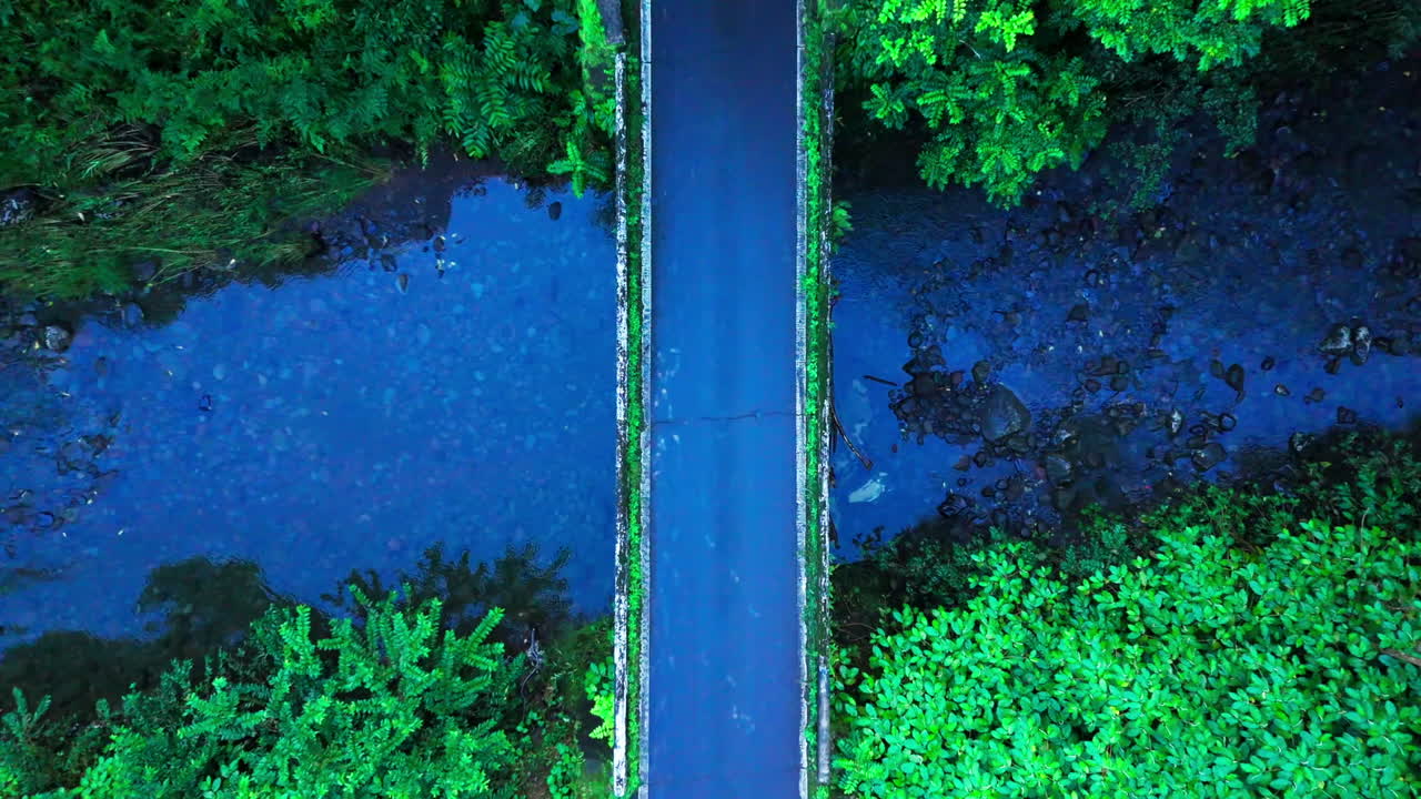 una toma aérea de un gran coche blanco conduciendo en un puente extremadamente estrecho que cruza en hawai durante un caluroso y tropical día de verano mientras exploraba la isla