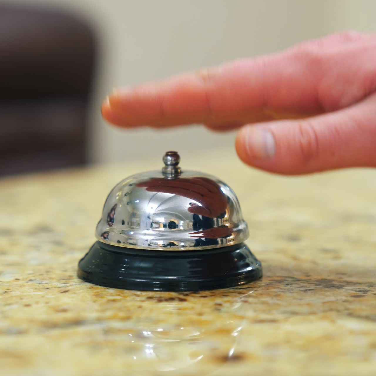 Metal bell button at hotel. Hand touching the electronic bell on the table to call a receptionist at a hotel. Close-up