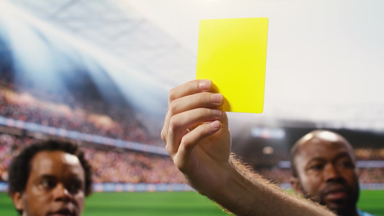 Close-up of yellow card held by referee hand after rules violation during match