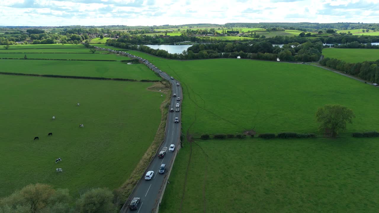 Smooth drone pass showing bridge structure, marsh vegetation and cars travelling on countryside route UK