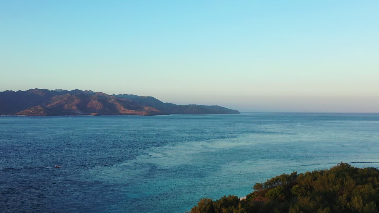 Cinematic view of scenery with dark blue sea between shores of islands in Indonesia, moments before sunrise with a bright sky background