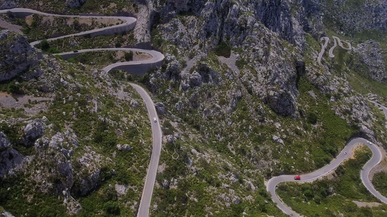 Riprese aeree di droni su strade di montagna tortuose mentre le auto si arrampicano su terreni rocciosi