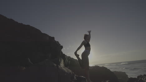 woman practicing yoga on a rocky beach at sunset