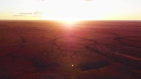 Toma-Aérea-De-Gran-Panorámica-De-Una-Increíble-Puesta-De-Sol-Sobre-Inmensas-Llanuras-De-Tierra-Roja-Del-Interior-Australiano