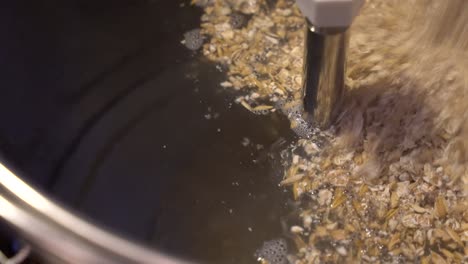 crushed malt is added to hot water in a stainless steel brew kettle for start of mashing process - close up view of beer making