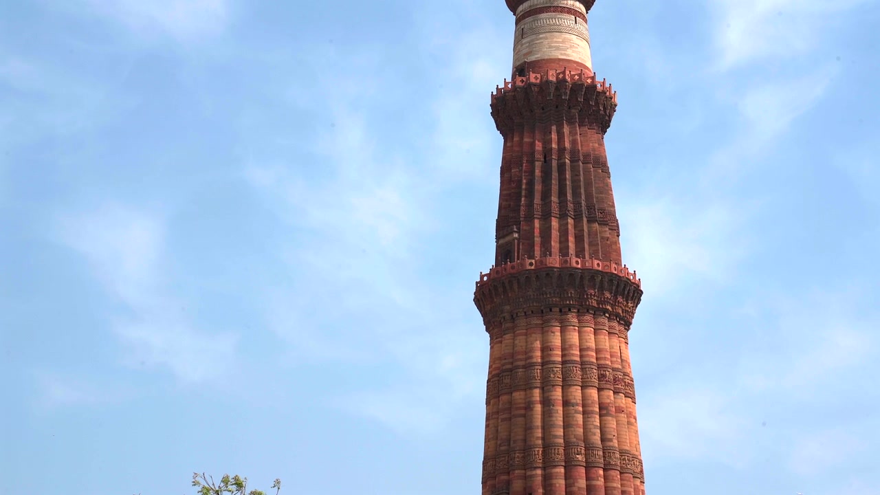 Statisk nærbillede i lav vinkel af de øverste balkoner og detaljerede udskæringer af Qutub Minar minareten mod en blå himmel i New Delhi, Indien.