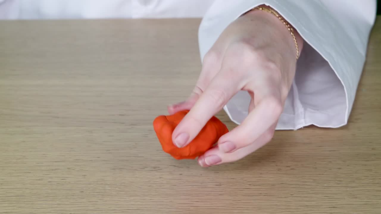 En person i en hvid laboratoriefrakke demonstrerer de fysiske egenskaber ved orange modellervoks
