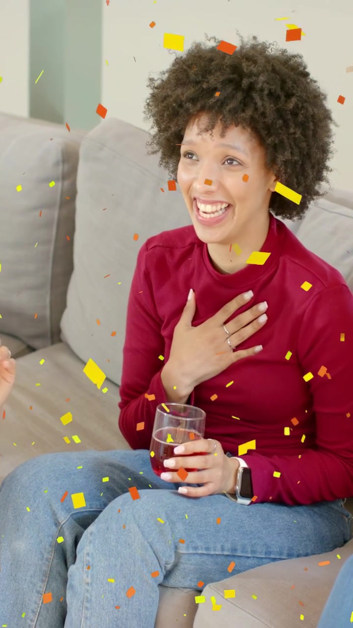 Video verticale: Donna con un bicchiere che reagisce all'amica che indica, ridendo, con coriandoli che cadono a una festa.