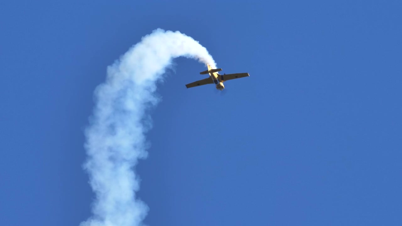 Gult lille fly udfører kunstflyvning på en klar himmel under et offentligt show. Flyver hurtigt på en solrig dag og udsender hvid røg bag flyet.