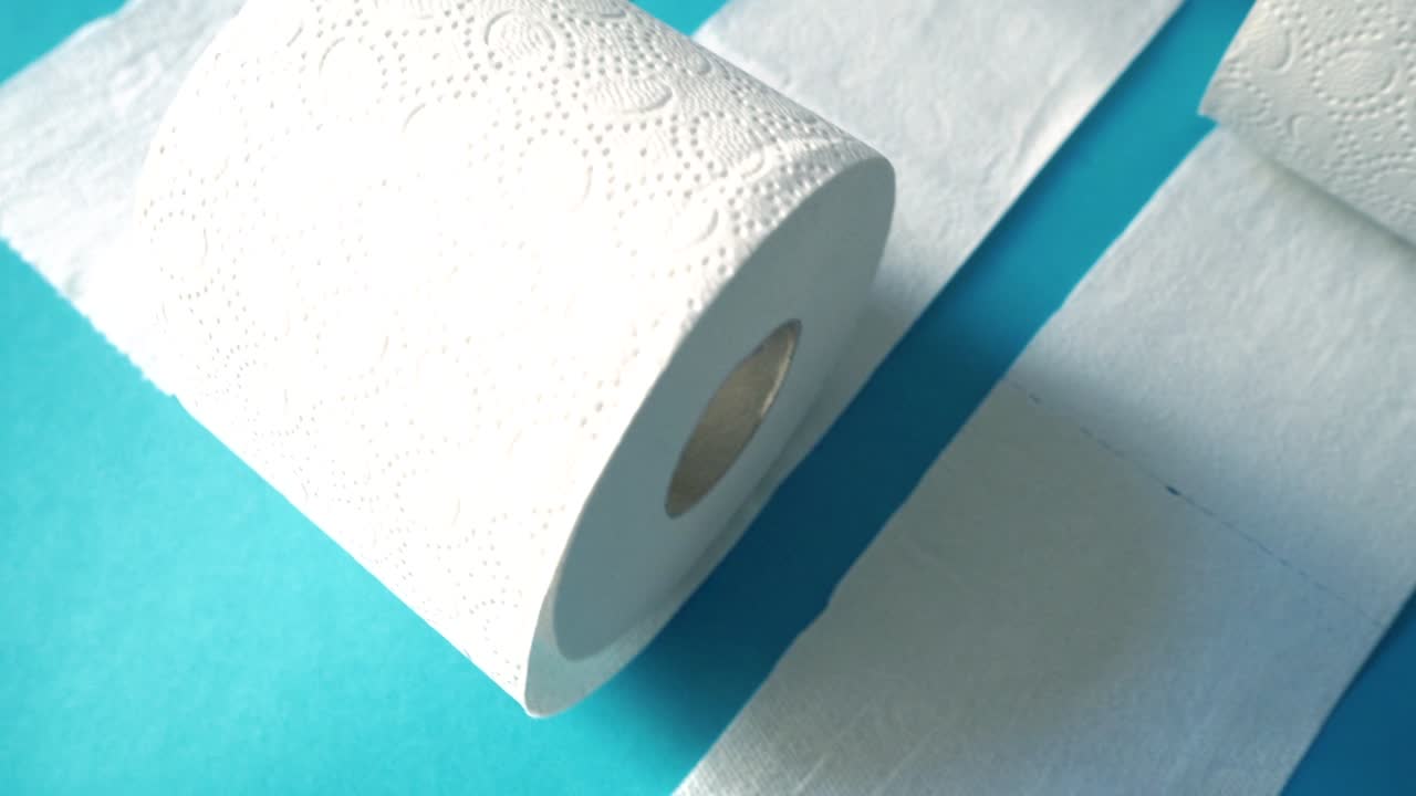 cámara lenta de varios rollos de papel higiénico contra un fondo moderno azul cian